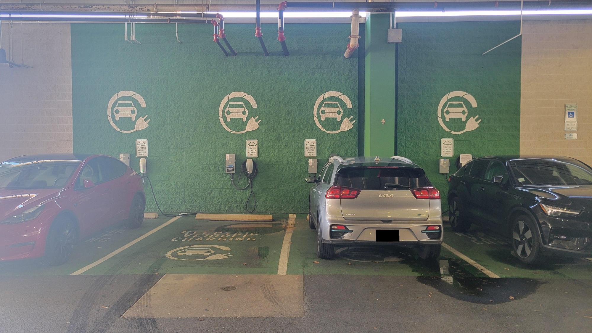 Shopping mall parking garage with green EV-only bays and wall-mounted chargers