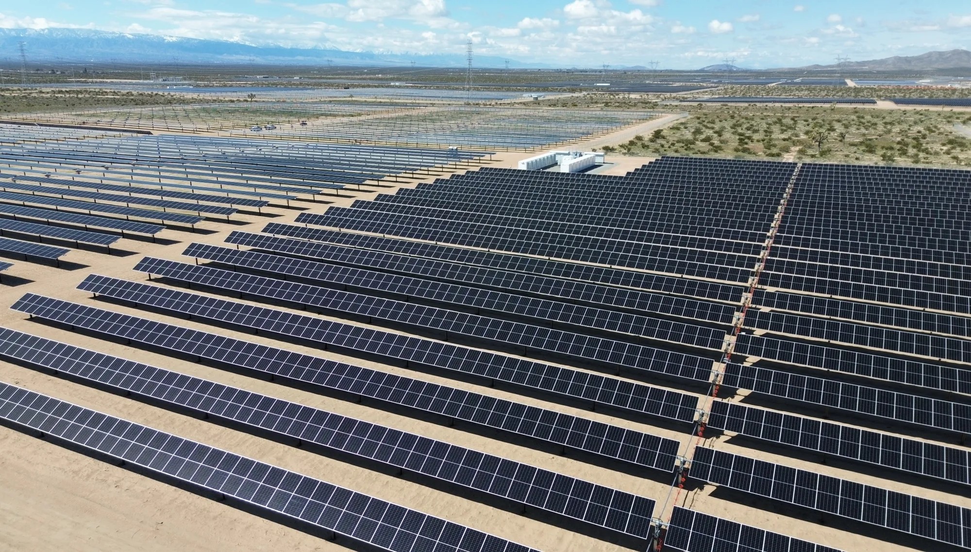 Large solar farm with rows of photovoltaic panels and an energy storage unit